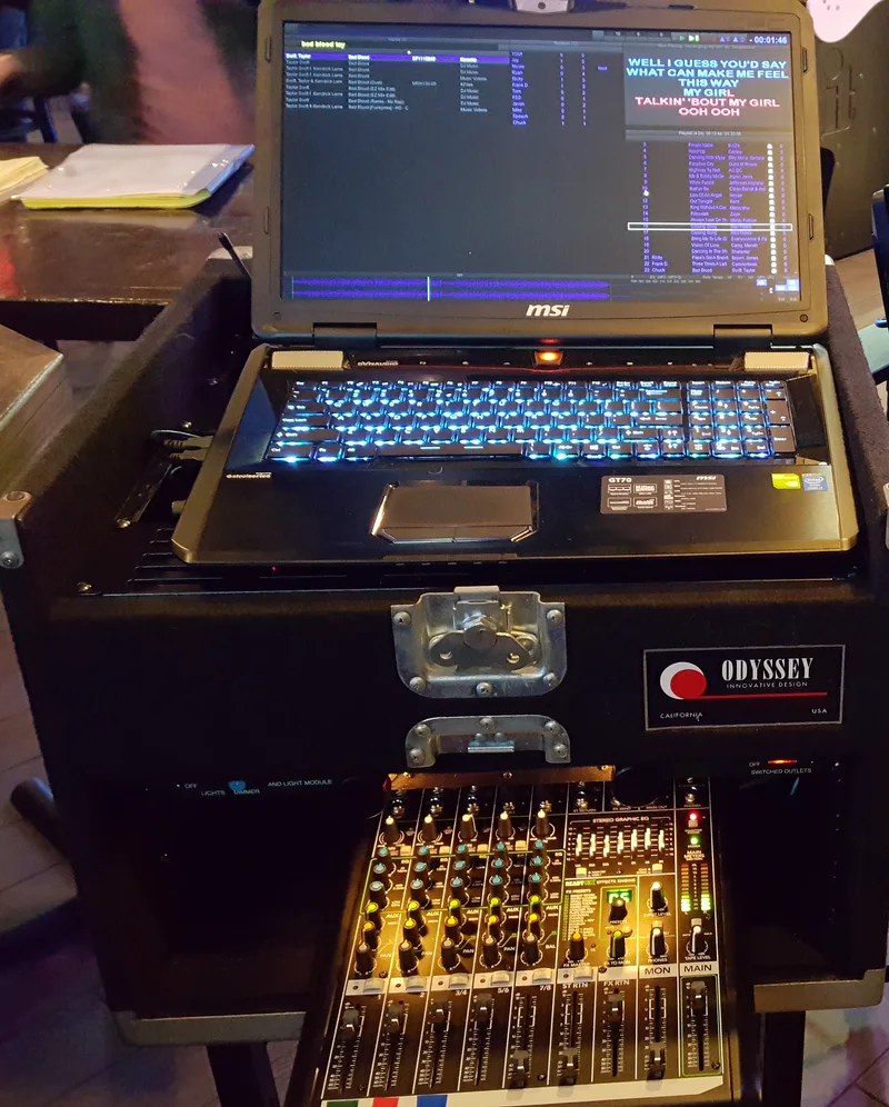 Close view of the karaoke DJ setup: laptop, illuminated keyboard, audio mixer and equipment case