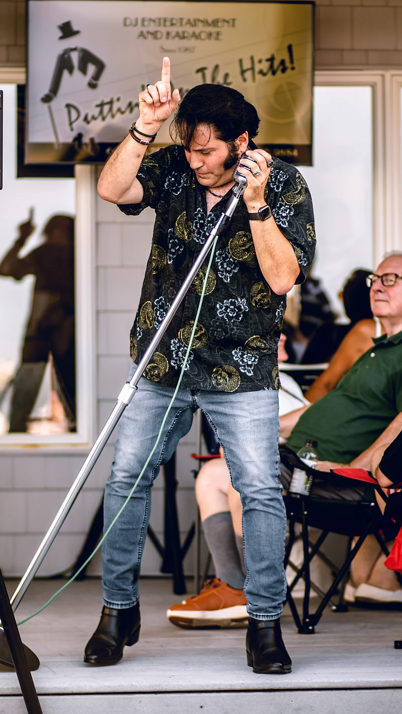 A guest singer performing at a hosted karaoke booking, in front of the Puttin' On The Hits display